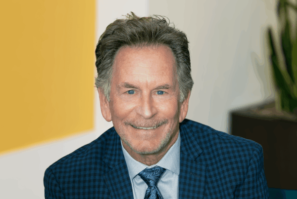 Smiling middle-aged man in a blue checkered suit and patterned tie; professional headshot.