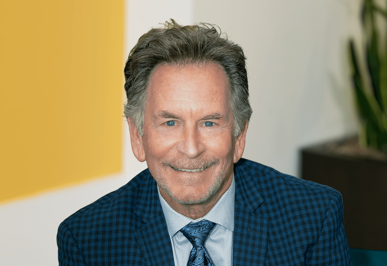 Smiling middle-aged man in a blue checkered suit and patterned tie; professional headshot.