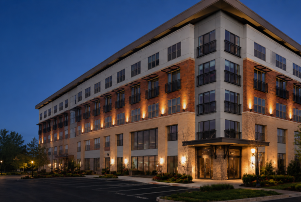 Modern four-story apartment building at dusk with brick and stone facade, warm exterior lights, and a front parking lot.